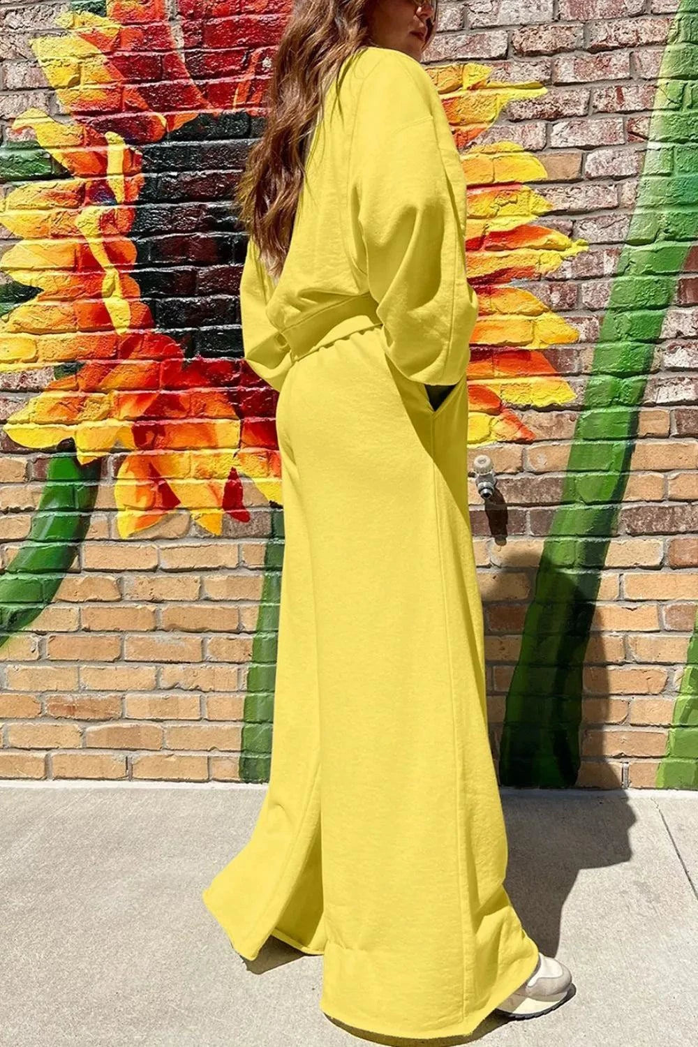 Woman wearing vibrant yellow round neck long sleeve sweatshirt and wide-leg pants set standing by sunflower mural