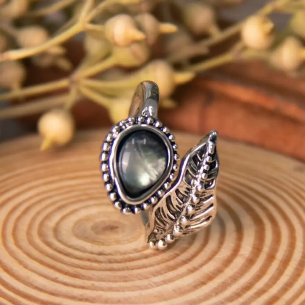 Alloy moonstone leaf bypass ring on wooden surface with dried botanical background