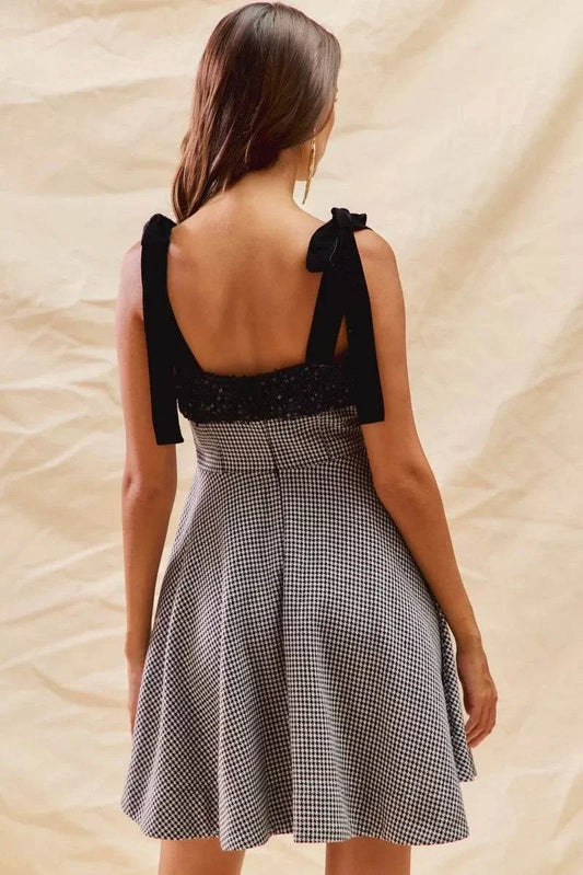 Back view of a woman wearing a houndstooth fit flare mini dress with black shoulder ties.