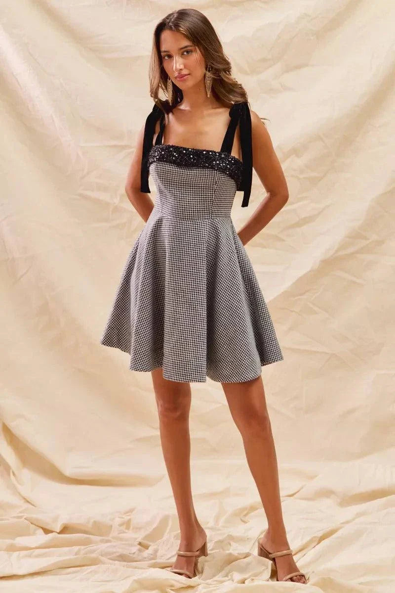 Woman wearing a houndstooth fit flare mini dress with black shoulder ties and a fitted bodice