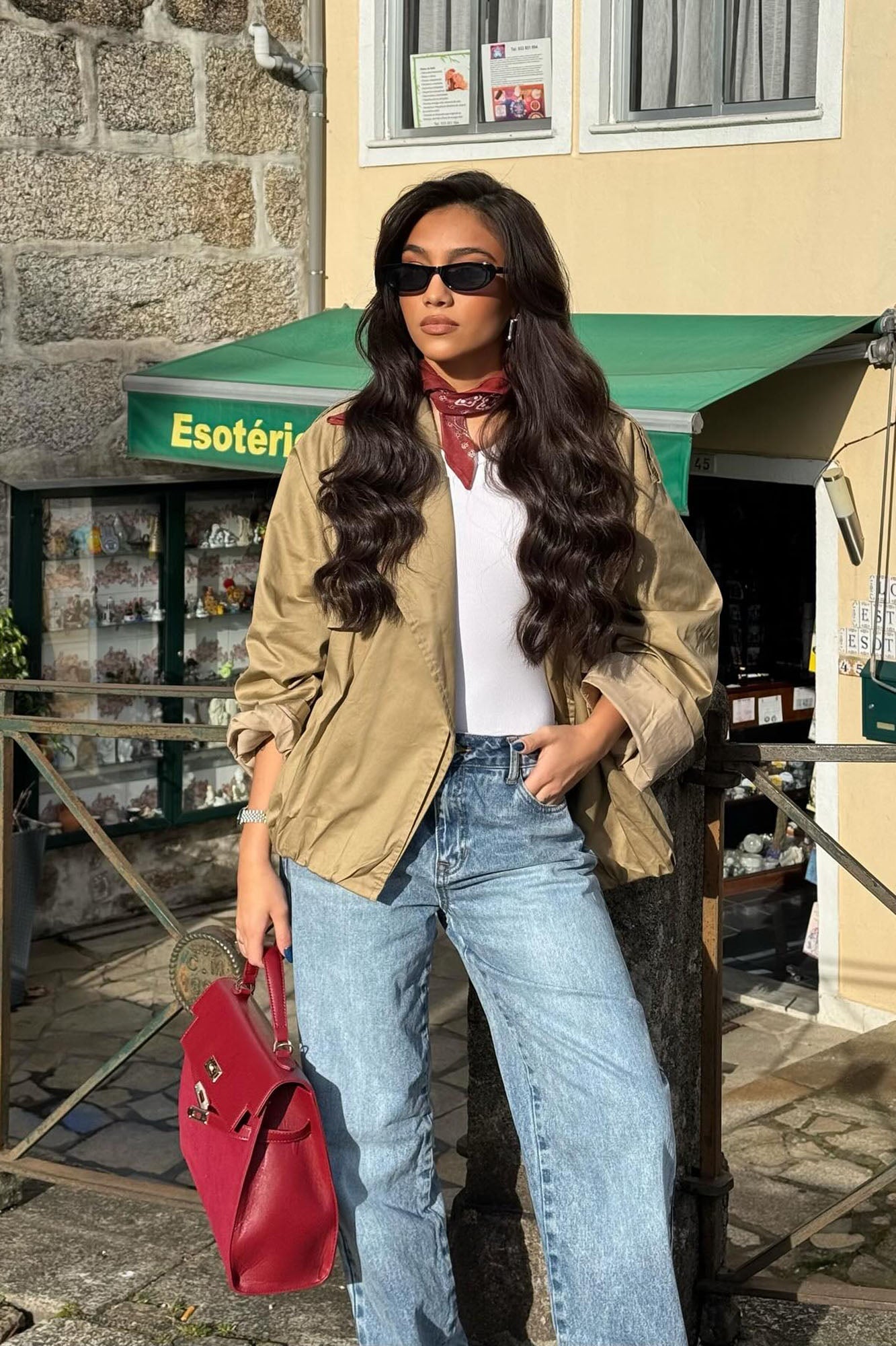 Fashionable woman wearing taupe Marie Cropped Bubble Trench with jeans and red handbag outdoors