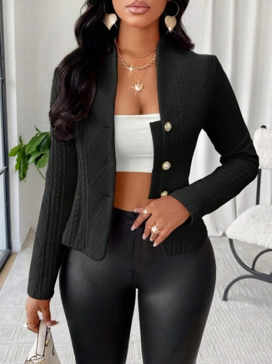 Woman wearing a black textured long sleeve jacket with pearl buttons and a white crop top indoors