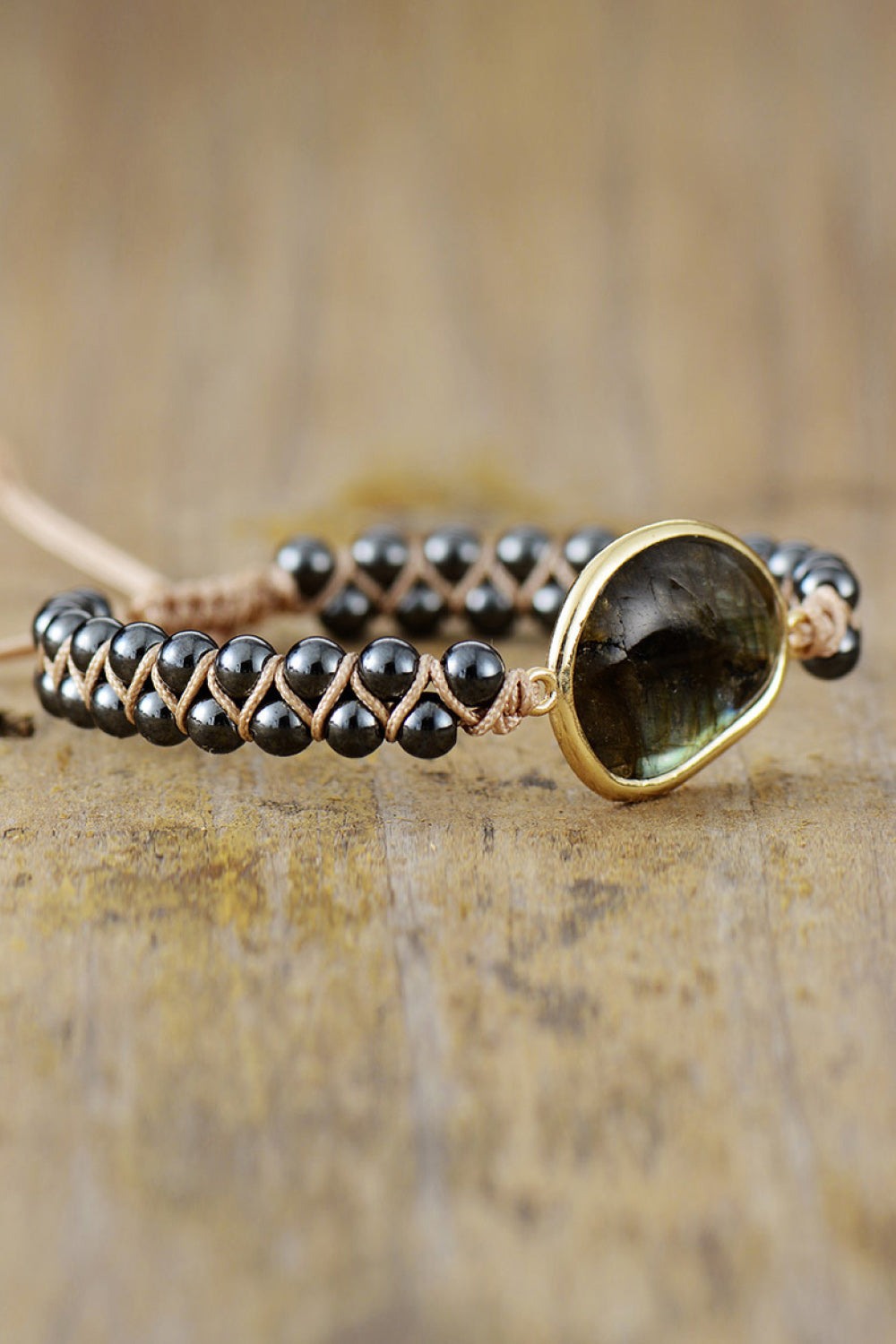 Natural stone beaded bracelet with black beads and a gold-framed central stone on wooden surface