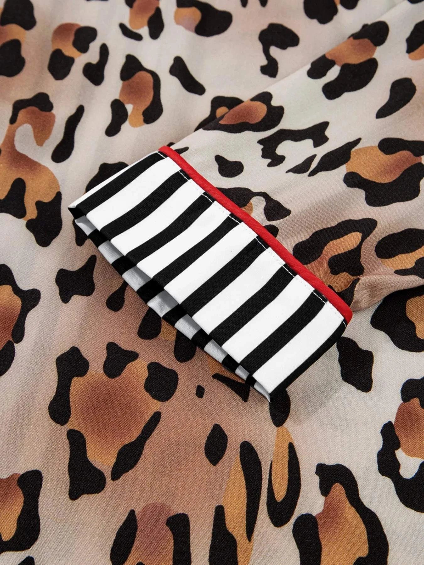 Close-up of leopard print fabric with black and white striped trim and red accent on shirt cuff