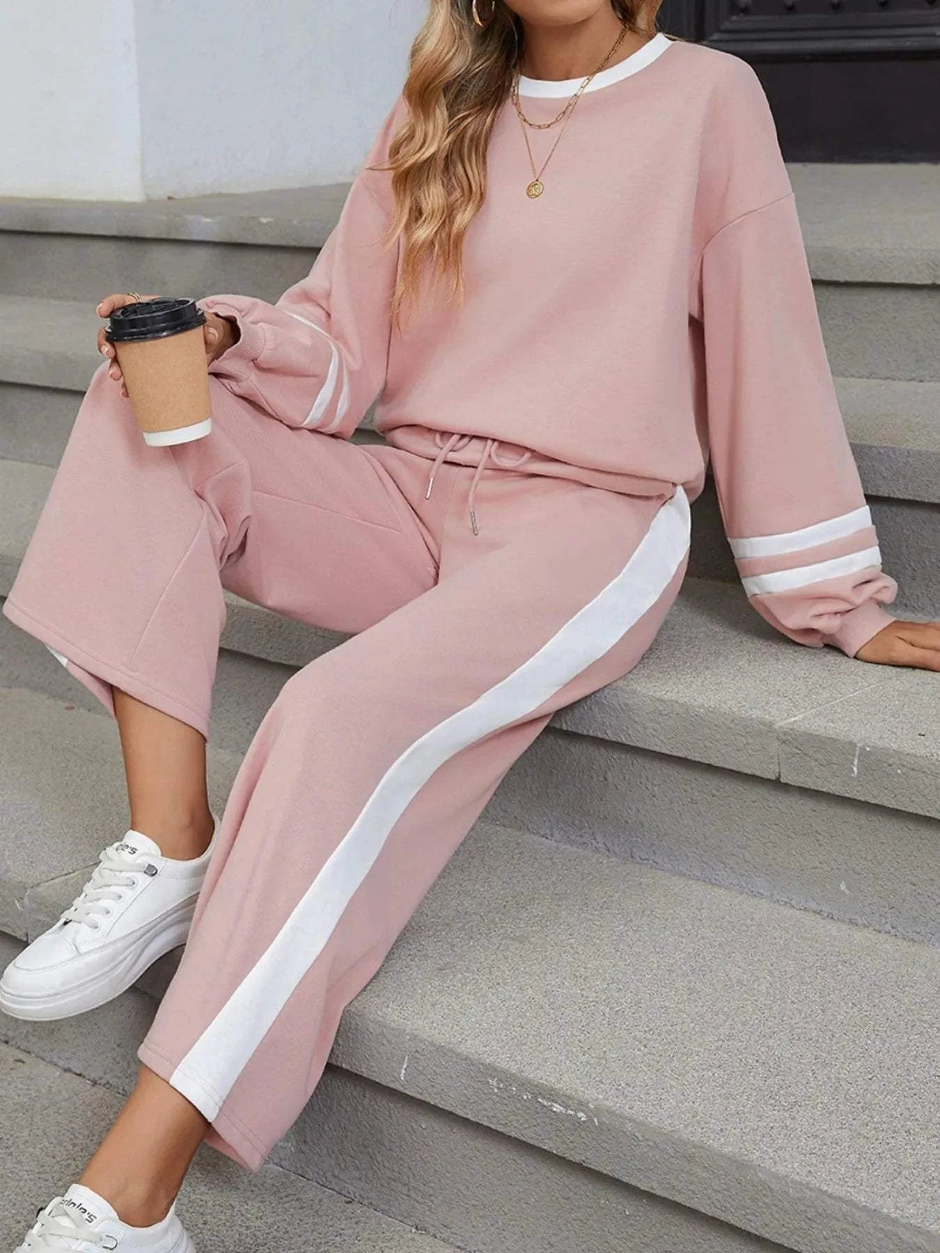 Woman wearing pink Contrast Trim Round Neck Top and pants set with white stripes and white sneakers sitting on steps holding a coffee cup