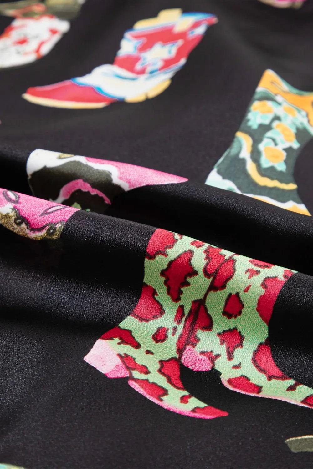 Close-up of printed fabric with colorful boot designs on a black background from a printed button up short sleeve top and shorts lounge set