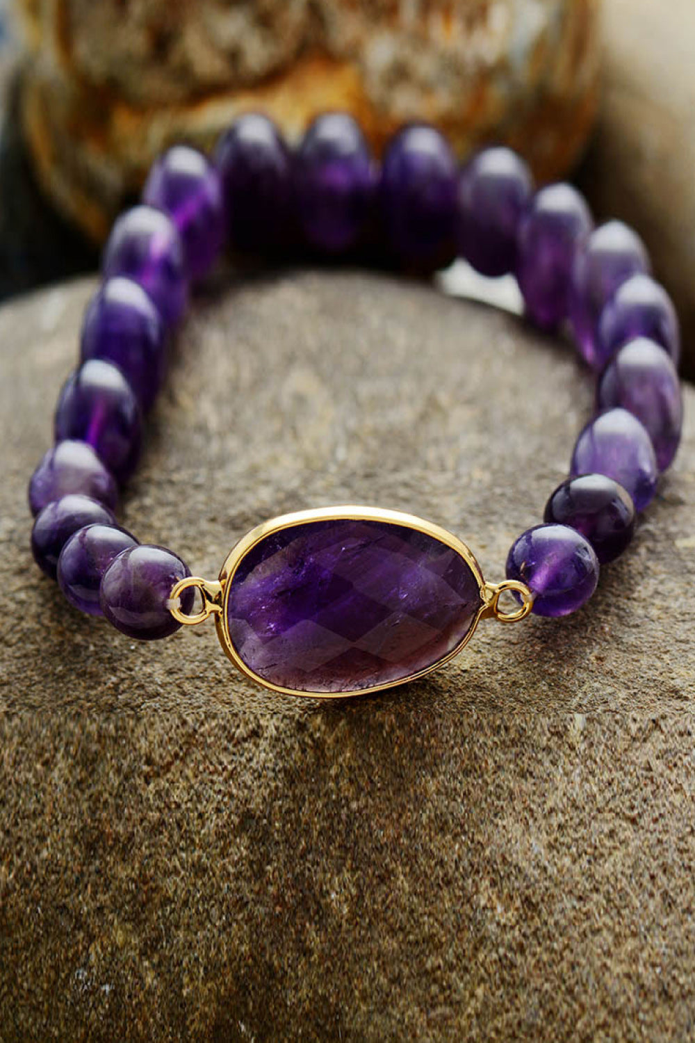 Handmade amethyst beaded bracelet with copper accents and oval centerpiece on stone background