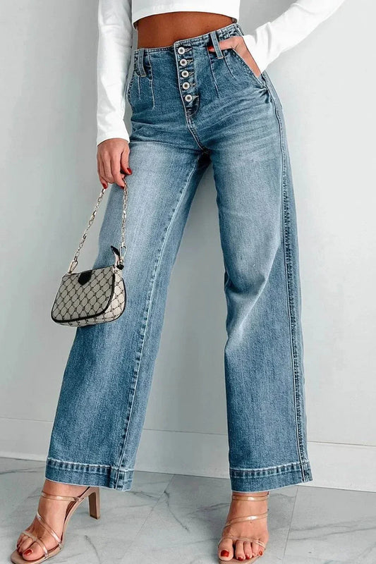 Woman wearing button fly high waist jeans with a cropped white top and heels, holding a small handbag.