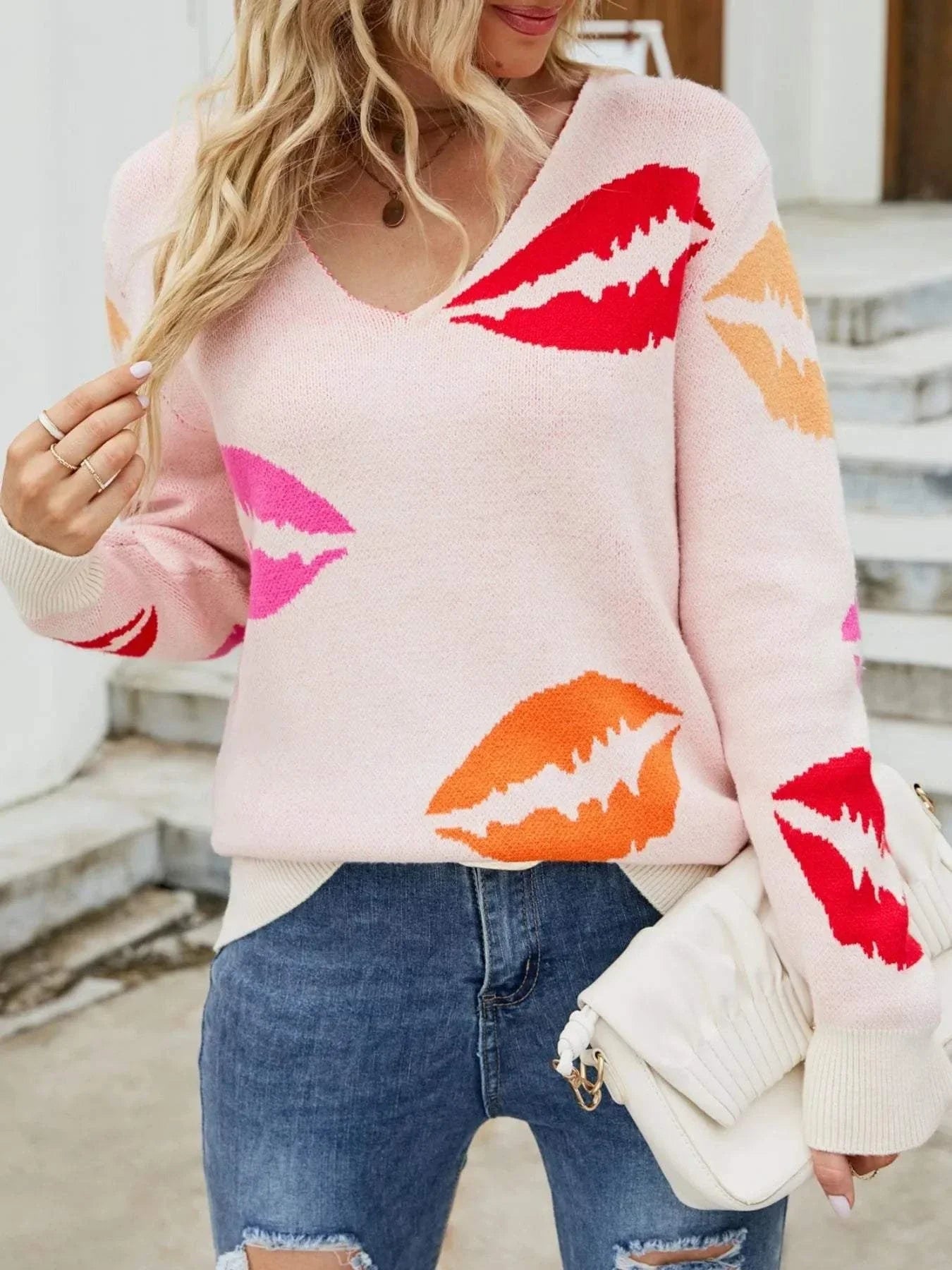 Woman wearing colorful V neck sweater with lip print paired with ripped jeans and a white clutch bag