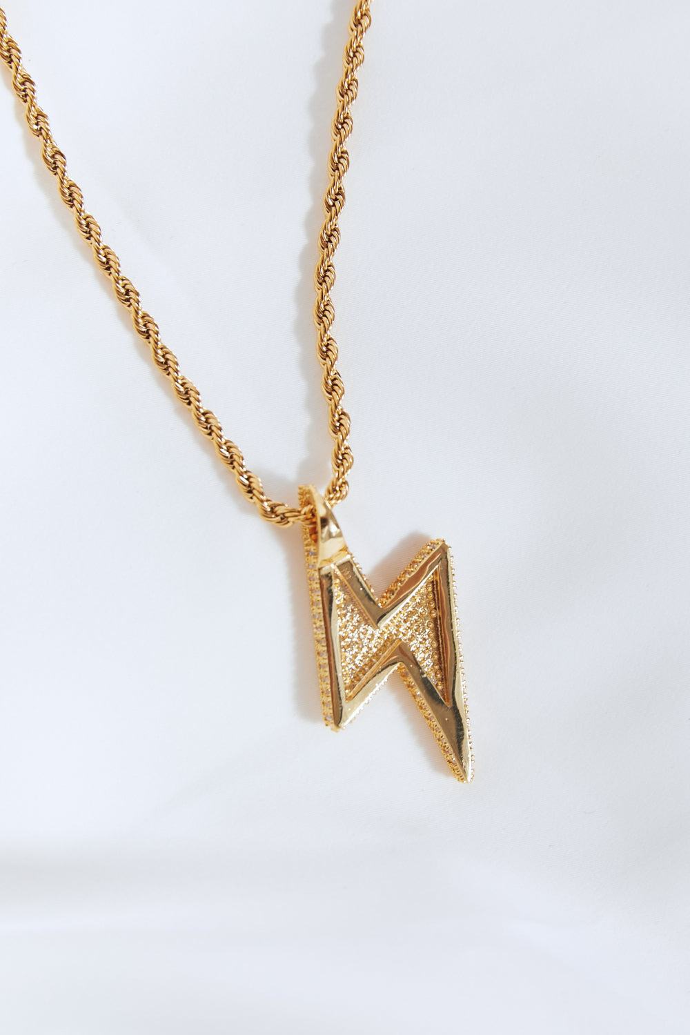 Close-up of brass lightning pendant necklace with twisted chain on white background