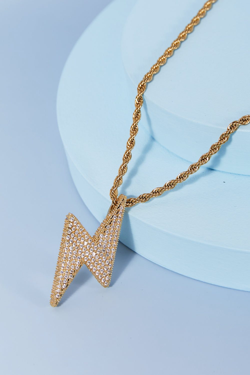 Brass lightning pendant necklace with crystal embellishments on a twisted chain against a light blue background