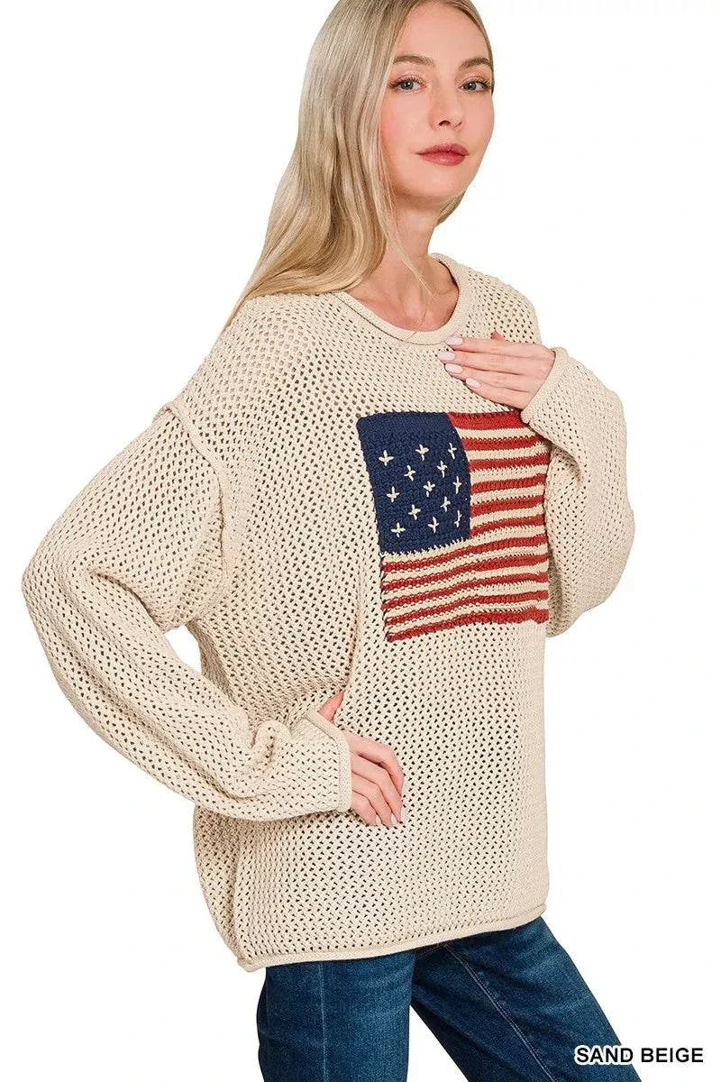 Woman wearing sand beige American flag crew neck sweater with openwork knit and ribbed cuffs paired with blue jeans