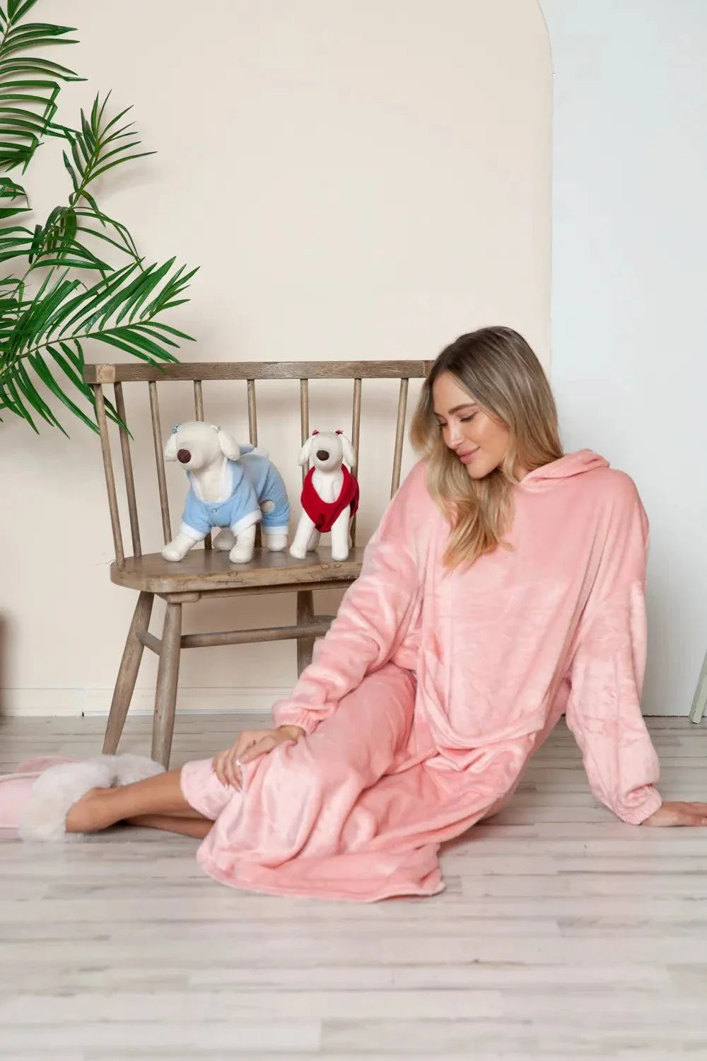 woman wearing pink hooded midi lounge dress sitting on floor next to wooden bench with stuffed dog toys