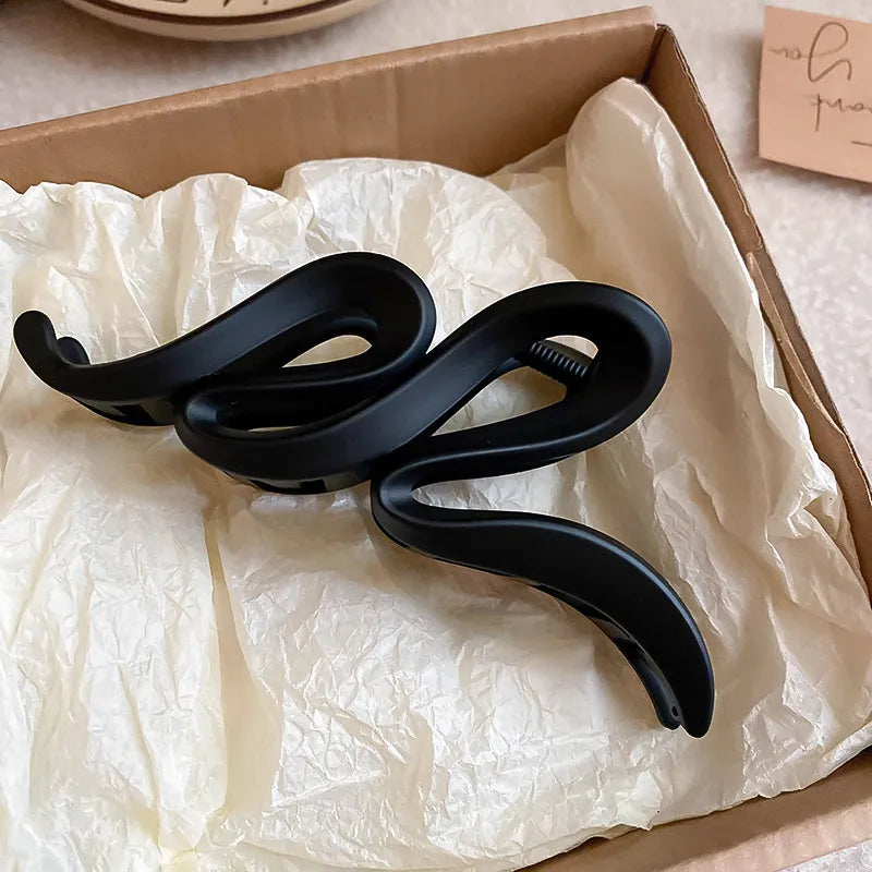 Black alloy acrylic hair claw clip with a wavy design, 5.2 inches long, placed on crumpled white tissue in a cardboard box