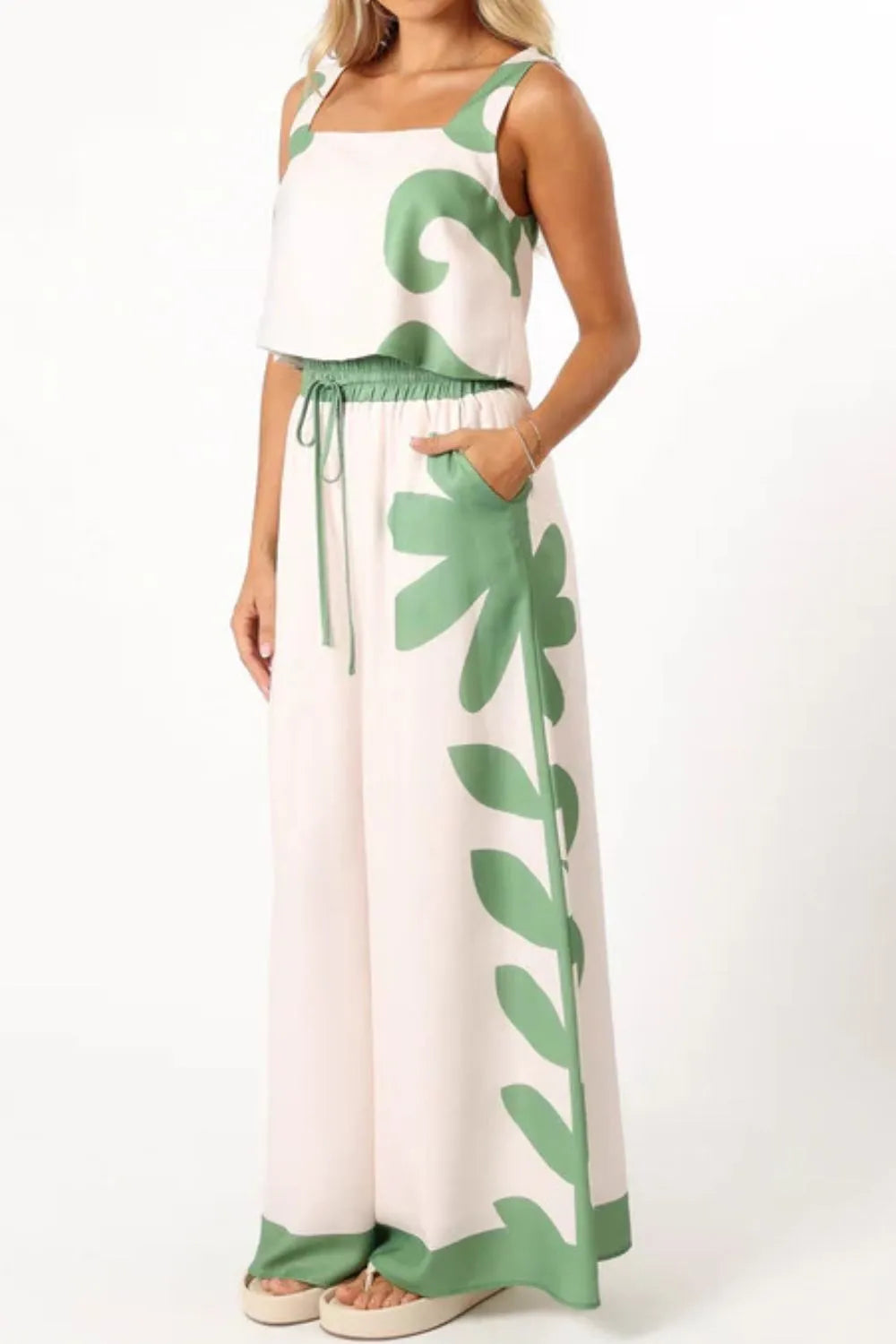 Woman wearing a white leaf print tank top and wide-leg pants set with green drawstring waist