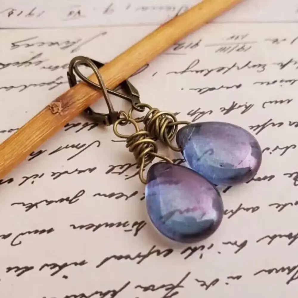 Alloy gemstone drop earrings with teardrop purple-blue stones and antique finish hooks on handwritten paper background