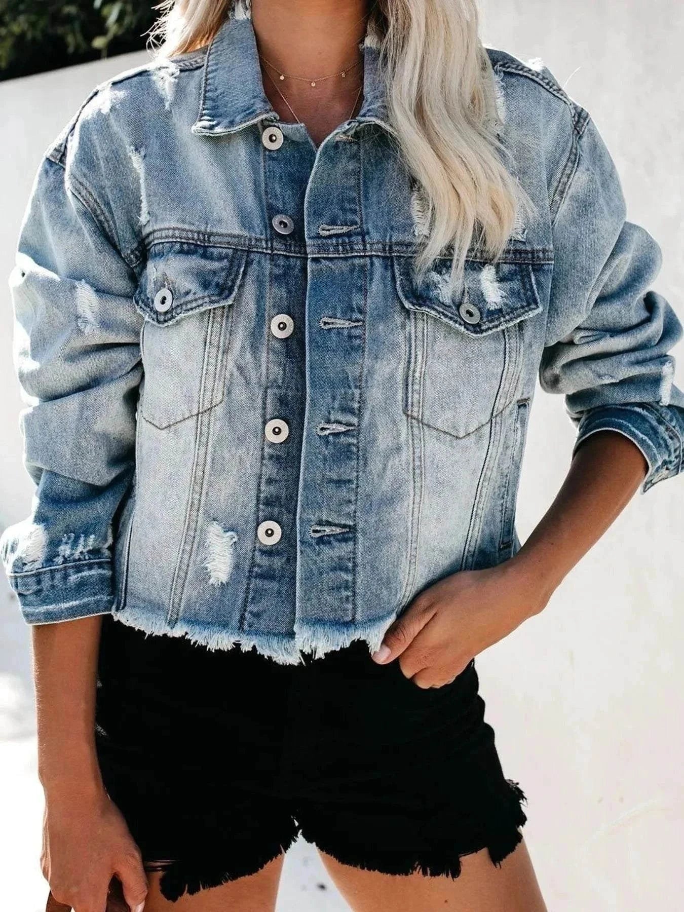 Woman wearing a light blue distressed denim jacket with raw hem and black shorts