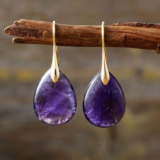Elegant crystal dangle earrings with purple teardrop stones hanging from gold hooks