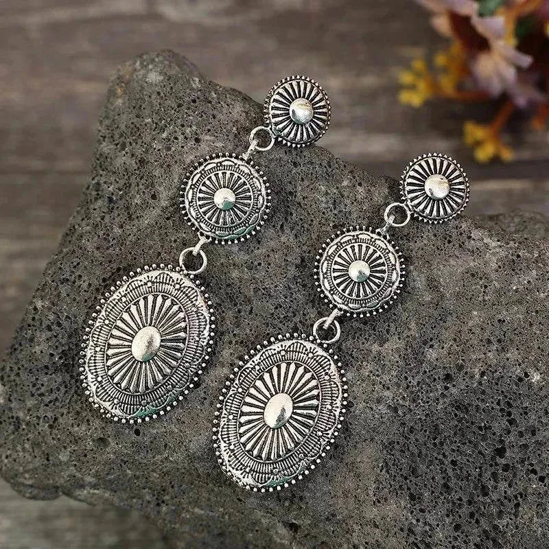 Vintage dangle earrings with intricate alloy design and antique silver finish on textured stone background