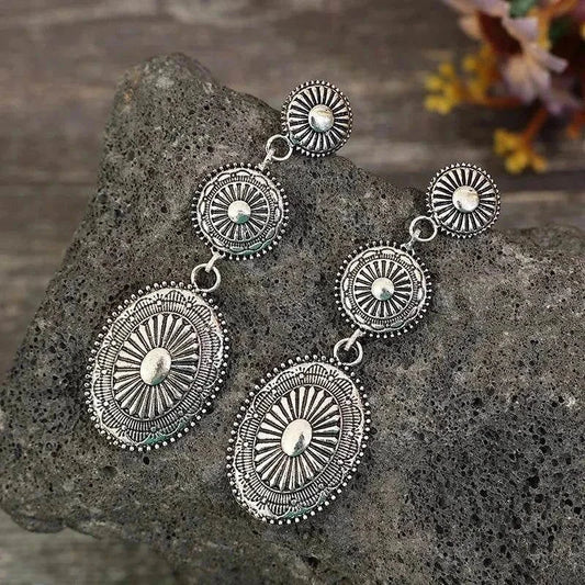 Vintage dangle earrings with intricate alloy design and antique silver finish on textured stone background