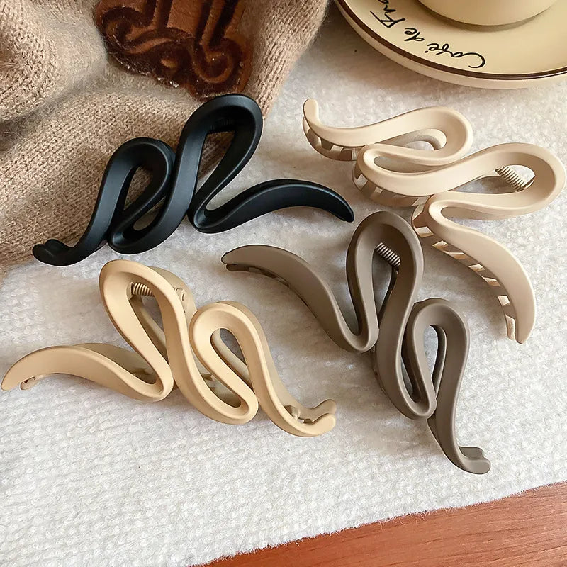 Set of alloy acrylic hair claw clips in black, beige, and gray colors on a white surface next to a coffee cup.
