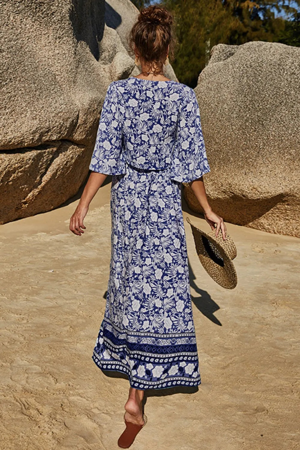 Woman wearing blue and white printed half sleeve top and slit skirt set walking on sandy beach with rocks in background