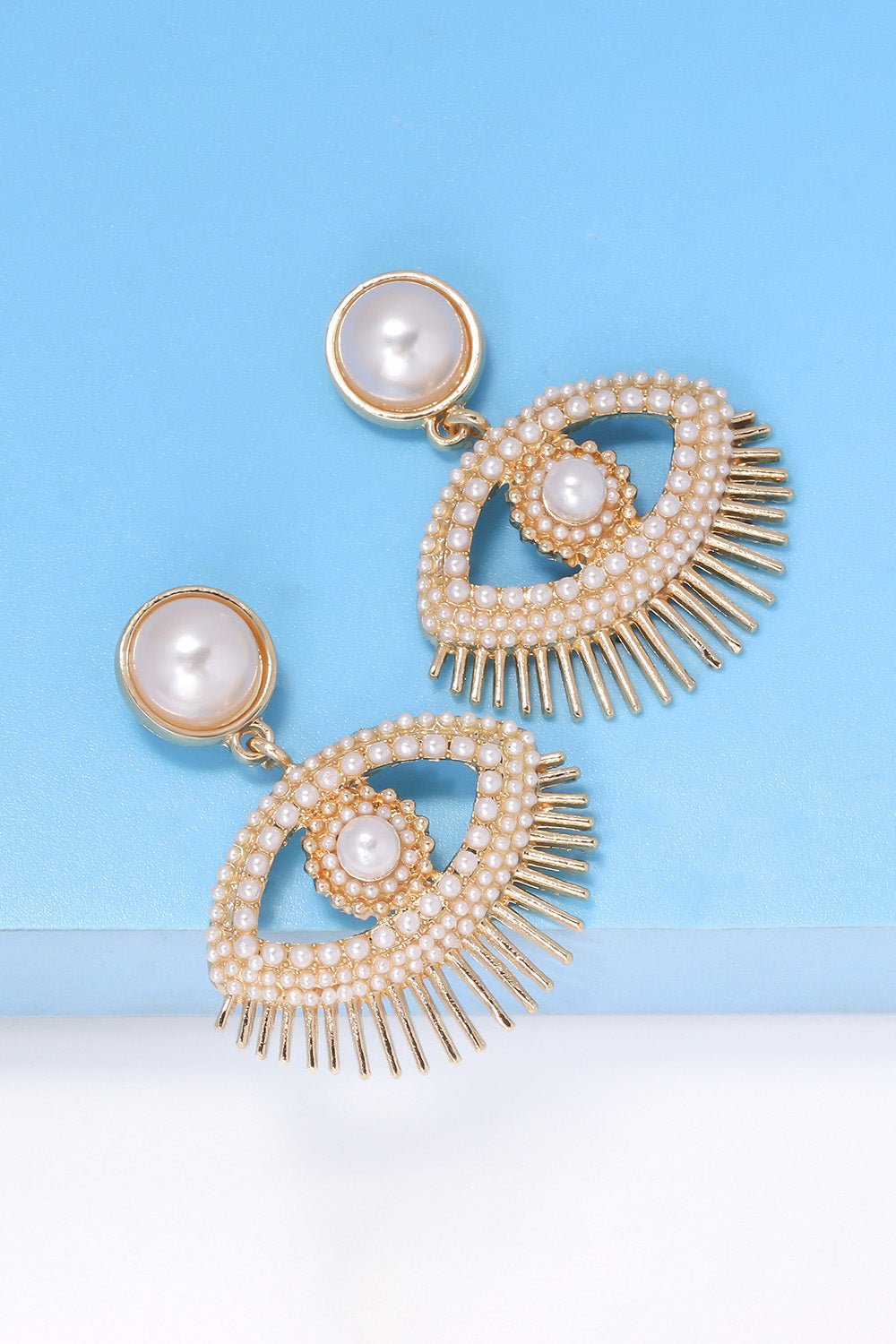 Evil eye shape rhinestone and synthetic pearl dangle earrings with gold zinc alloy accents on blue background