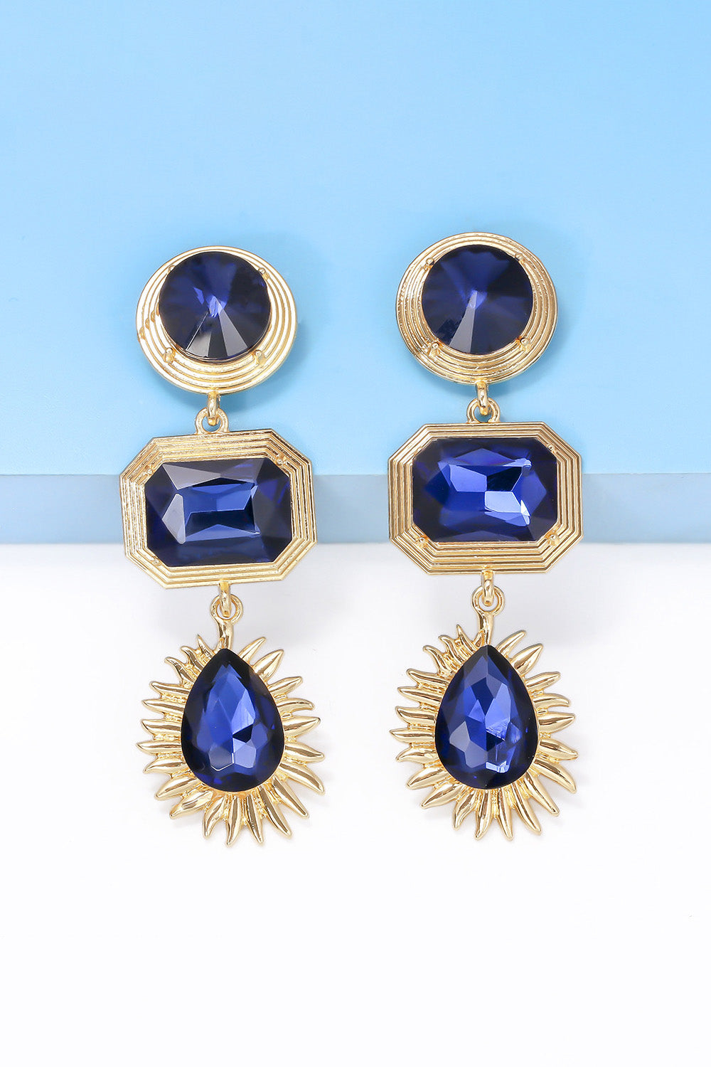 Geometrical shape zinc alloy frame dangle earrings with blue glass stones on blue background