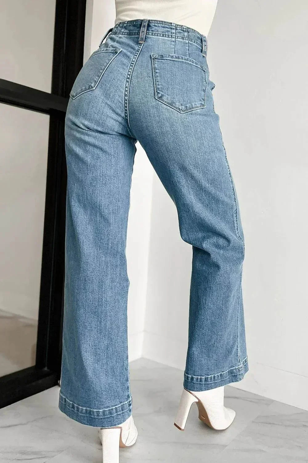 Rear view of woman wearing light blue button fly high waist jeans and white high heel shoes