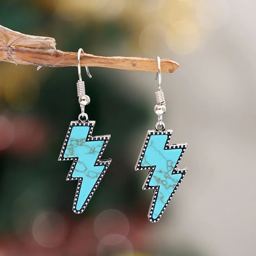 Artificial turquoise lightning bolt dangle earrings with silver-plated alloy detailing hanging on branch