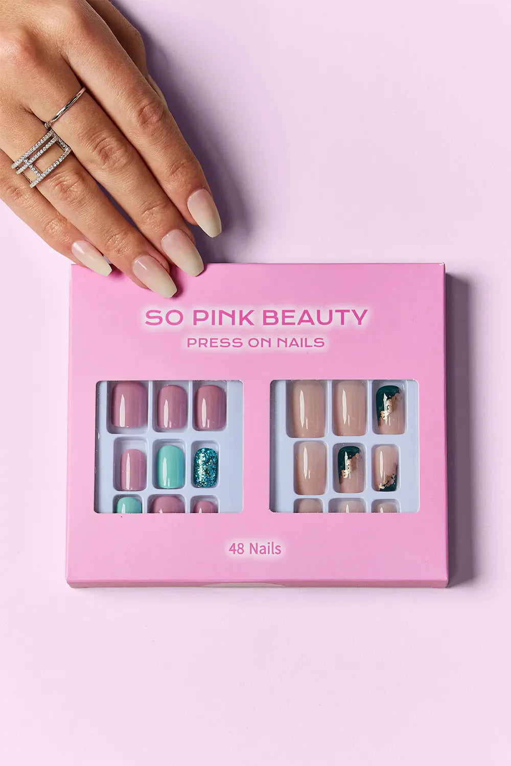 So Pink Beauty Press On Nails two-pack with 48 pieces including pink, teal, glitter, and marble designs in a pink box with hand model showing applied nails