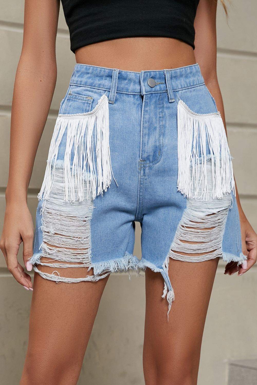 Fringe trim distressed denim shorts with large white fringe pockets and frayed hems.