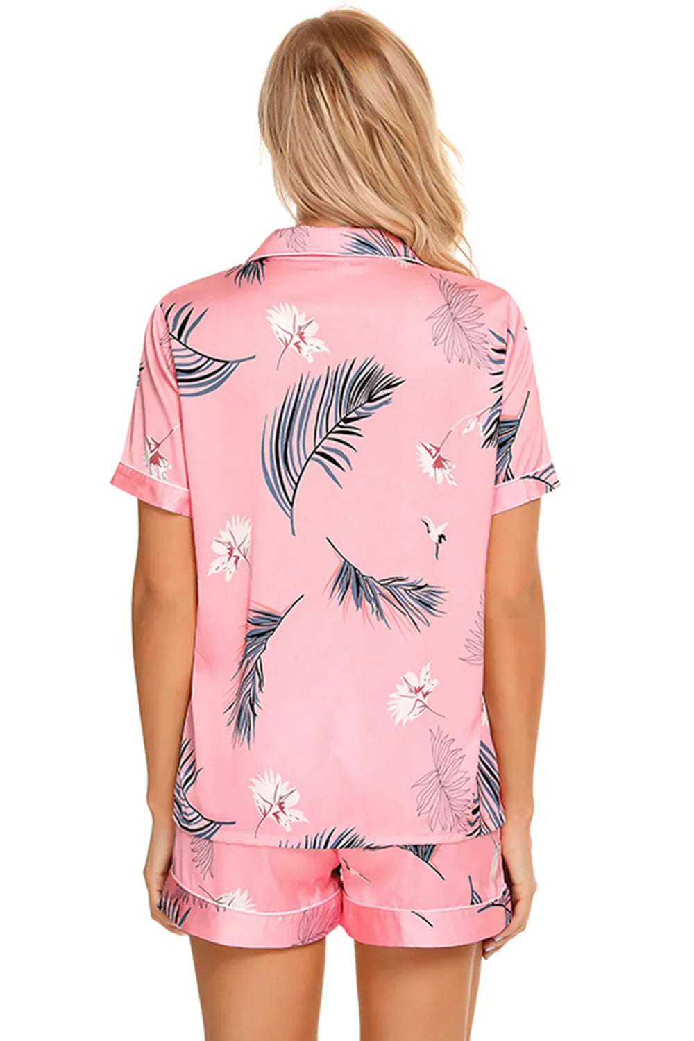 Back view of a woman wearing a pink printed button up short sleeve top and shorts lounge set with floral and leaf patterns