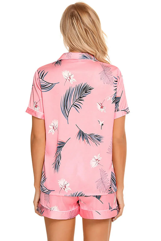 Back view of a woman wearing a pink printed button up short sleeve top and shorts lounge set with floral and leaf patterns