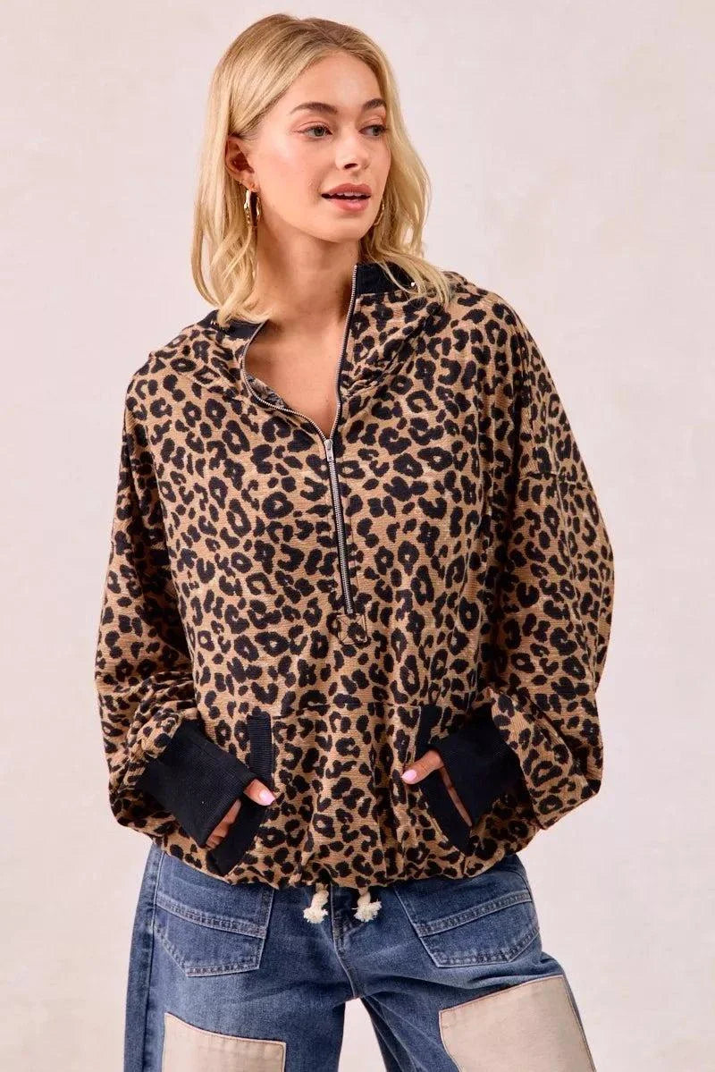 Woman wearing a leopard print waffle half zip up hoodie with pocket and black cuffs paired with patchwork jeans