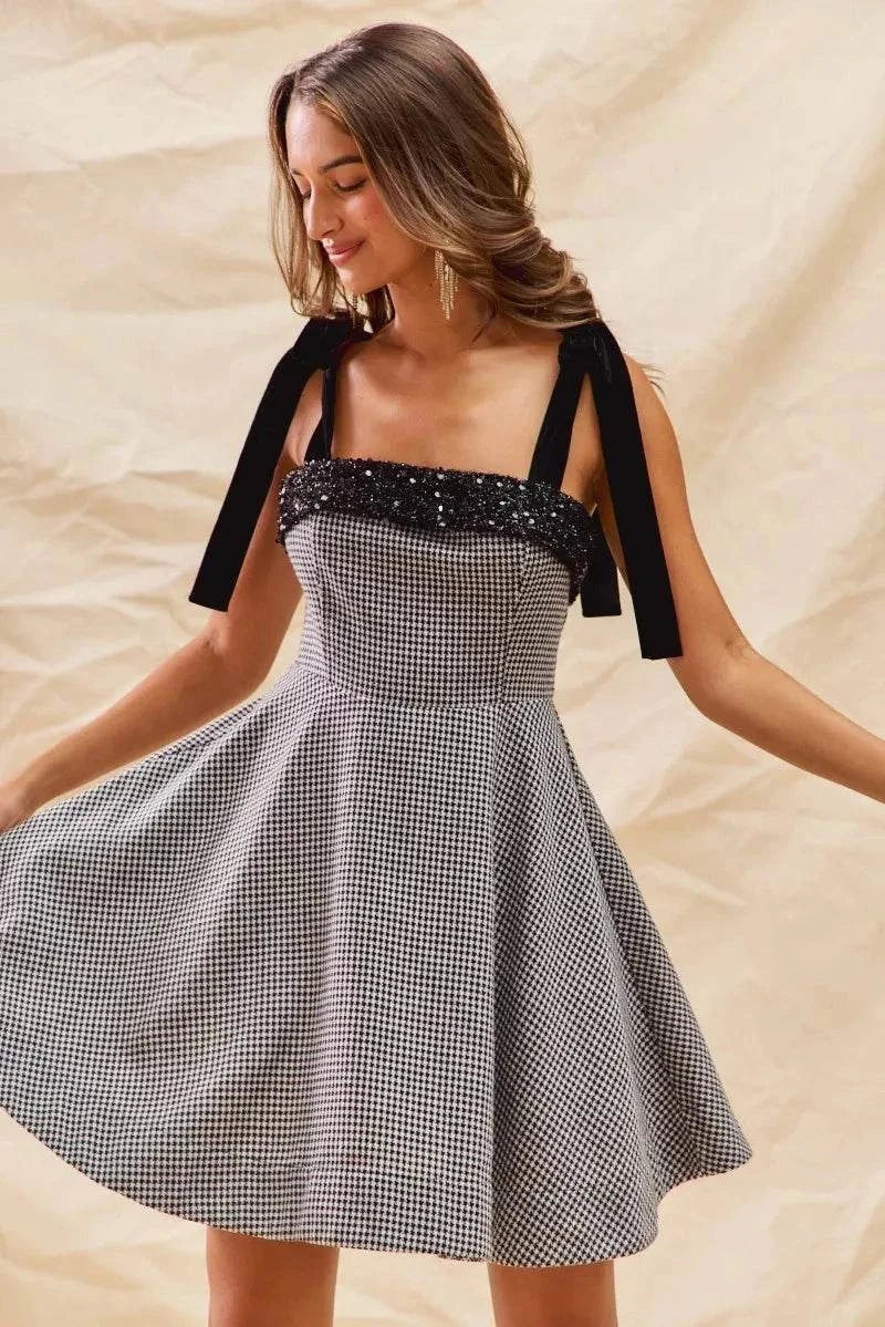 Woman wearing a houndstooth fit flare mini dress with black shoulder ties and sequin detailing