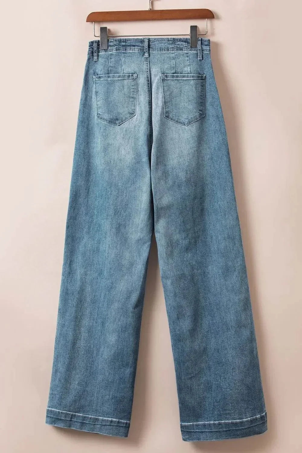 Back view of light blue Button Fly High Waist Jeans hanging on wooden hanger against beige background