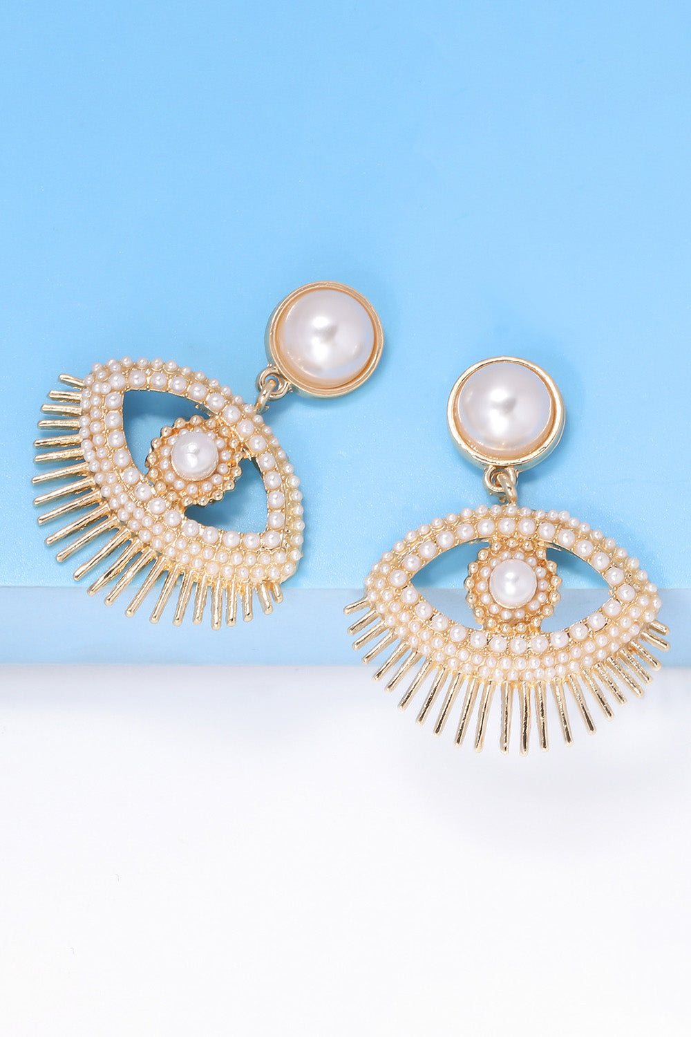 Evil eye shape rhinestone and synthetic pearl dangle earrings with zinc alloy frame on blue background